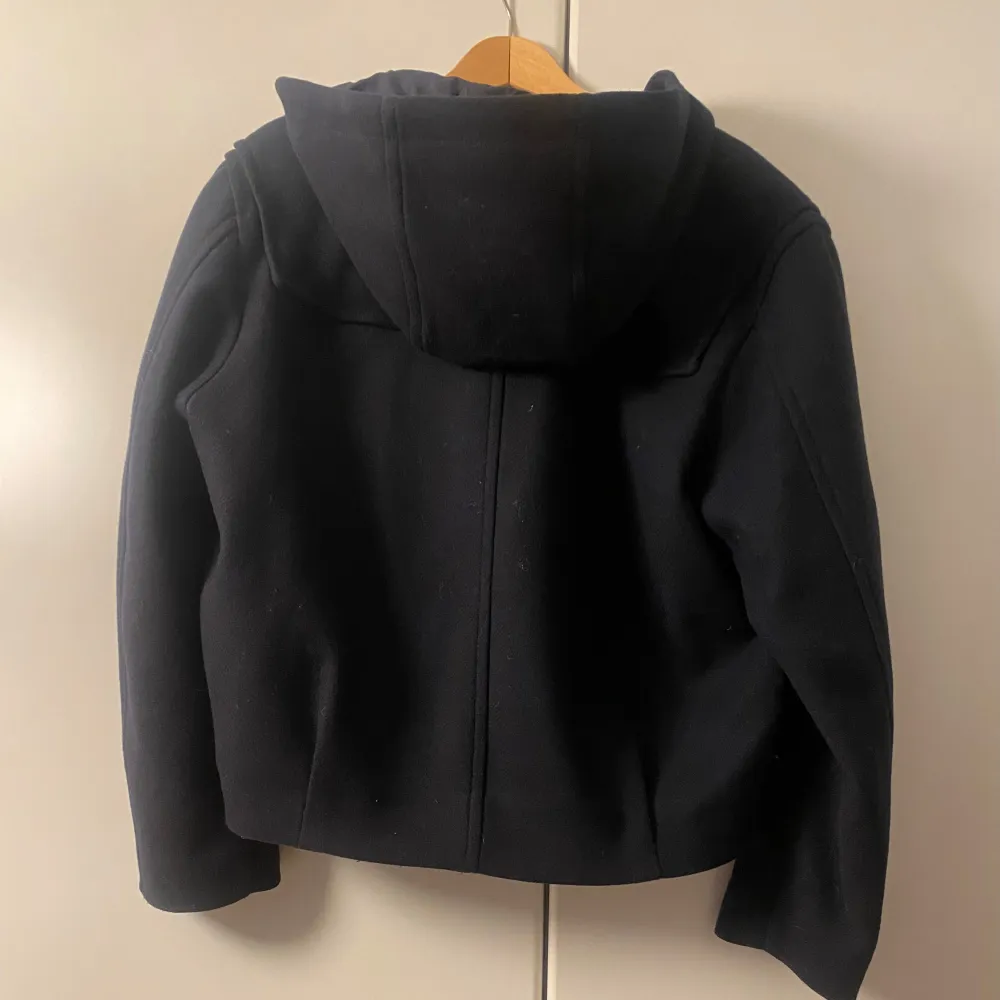 Säljer en snygg mörkblå jacka från Zara i mycket bra skick. Knappt använd då den inte riktigt är min stil. Den har en praktisk huva och stängs med både dragkedja och knappar. Jackan har långa ärmar och stora fickor framtill.. Takit.