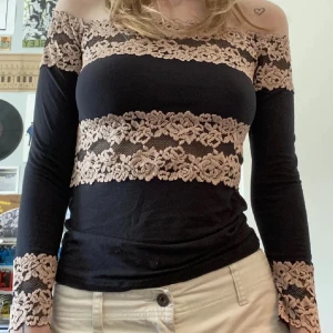 Svart offshoulder topp med spetsdetaljer - Säljer en snygg svart offshoulder topp med vackra beige spetsdetaljer. Toppen har långa ärmar och en tight passform, perfekt för både fest och vardag. Den är i mycket bra skick och ger en elegant touch till vilken outfit som helst. Är från intimissmi❤️