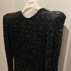 Svart glittrig klänning från Valentino - Säljer en fantastisk svart glittrig klänning från zara. Den har en djup v-ringning och långa ärmar, perfekt för festliga tillfällen. Klänningen är täckt av paljetter som ger en glamorös look. Ny med taggar kvar!