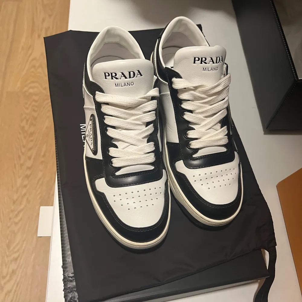 Säljer ett par snygga svartvita sneakers från Prada i mycket bra skick. De har en klassisk design med Pradas logga på sidan och är perfekta för både vardag och fest. Skorna har snörning och en bekväm sula som ger bra stöd. Perfekta för dig som vill ha stil och komfort i ett! Kvitto finns för seriösa köpare. . Kengät.