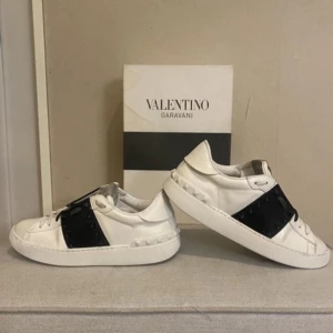 Valentino Garavani sneakers - Säljer ett par snygga Valentino Garavani sneakers i vitt skinn med svarta detaljer. Skorna har den ikoniska rockstud-designen och är i mycket bra skick. Perfekta för både vardag och fest! Storlek 37