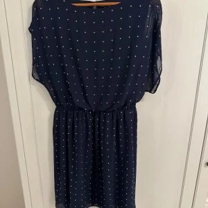 Mörkblå prickig klänning från  Warehouse - Säljer en superfin mörkblå klänning med små guldiga prickar från  Warehouse. Den har en bekväm passform med resår i midjan och korta ärmar. Perfekt för både vardag och fest! 💙