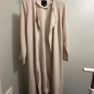 Säljer en stilren beige trenchcoat från 157 i storlek L. Den har långa ärmar och ett bälte i midjan för en snygg passform. Perfekt för vår och höst! Den är helt oanvänd! 