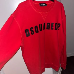 Röd sweatshirt från Dsquared2 - Säljer en snygg röd sweatshirt från Dsquared2 i storlek XL. Tröjan har ett coolt tryck med märkesnamnet på framsidan. Perfekt för en avslappnad stil och passar bra till både jeans och joggers. Tillverkad i Italien och i mycket bra skick. Perfekt för höst och vår! (XL men passar även som L)