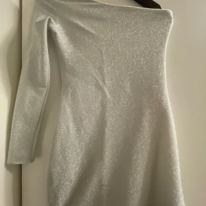 Glittrig silverklänning - Säljer en superfin glittrig silverklänning från hm i storlek XS. Klänningen har en elegant off-shoulder design och långa ärmar, perfekt för en festlig kväll eller bal. Materialet är stretchigt och bekvämt, vilket gör den både snygg och lätt att bära. ✨
