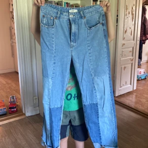Blå jeans från Pull&Bear - Säljer ett par snygga blå jeans från Pull&Bear i storlek L. De har en cool patchwork-design med olika nyanser av blått och är högmidjade. Perfekta för en avslappnad och trendig look! De är i bra skick och redo för en ny ägare.