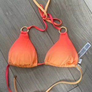 Orange och gul bikiniöverdel - Säljer en superfin ny bikiniöverdel i en härlig ombre av orange och gul. Den har knytband i nacken och ryggen, samt snygga guldringar som detaljer. Perfekt för sommarens alla bad och strandhäng! 🏖️
