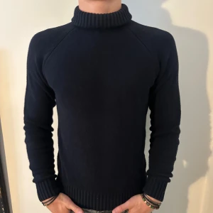 Mörkblå stickad polotröja med Turtleneck krage - Säljer en snygg och stilren Mörkblå stickad polotröja. Tröjan har långa ärmar och en ribbad Turtleneck krage samt muddar vid ärmslut och nederkant. Tröjan är i så gott som nytt skick! Modellen är 182 cm och väger 75 kg. Pris går att diskuteras!