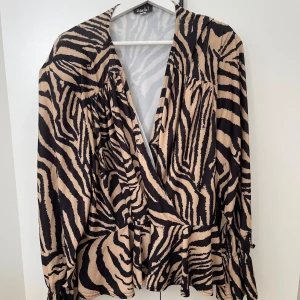 Mönstrad blus dam - Omlott färgad blus i svart och brun/beige i storlek xxl.  Peplumtopp med vida armar och knytband samt små axelkuddar.  Knappast använd, väldigt fint skick. 