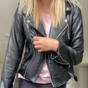 Svart skinnjacka från Zara - Säljer en snygg svart skinnjacka från Zara i storlek S. Jackan har en klassisk bikerstil med dragkedjor och knappar som detaljer. Den har också ett bälte i nederkanten för en extra cool look. Perfekt för höst och vår! knappt använd
