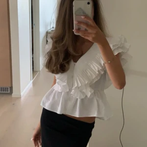 Vit volangblus från Zara - Säljer en superfin vit blus från Zara med volangdetaljer. Blusen har en v-ringad hals och korta ärmar med volanger. Helt ny med tag kvar. 🫶🏼🫶🏼