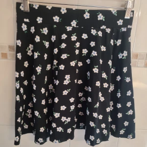 Svart blommig kjol  - Jättefin svart kjol med vita/blåa blommor. Material: 95% bomull och 5% elastan, stretchig I midjan. 