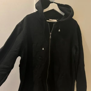 Svart zip hoodie - Säljer min svarta zip hoodie från Lindex. Den har en knytning så man kan spänna den vid midjan som jag gjort på mina bilder.🌸 Oklar storlek då lappen klippts av men tycker den sitter som en L/oversized M🩷
