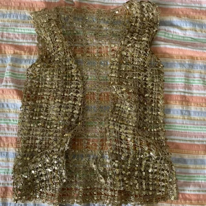 Guldig paljettväst - Säljer en superfin guldig väst med paljetter. Västen är öppen framtill och har ett glittrigt nätmönster. Perfekt för fest eller en glammig utekväll! 
