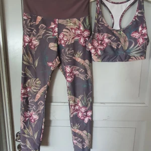 Blommigt träningsset från Energetics - Säljer ett snyggt och bekvämt träningsset från Energetics i storlek XS. Setet består av en sport-bh och leggings, båda med ett vackert blommigt mönster i rosa och gröna nyanser på en mörk bakgrund. Materialet är polyester med DryPlus eco-teknologi som håller dig torr under träningen. Perfekt för gymmet eller yoga!