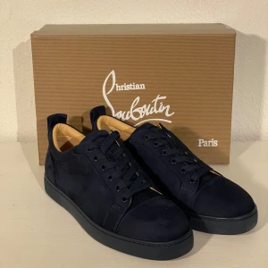 Mörkblå sneakers från Christian Louboutin - Snygga mörkblå sneakers i mocka från Christian Louboutin med den ikoniska röda sulan. Skorna har snörning och en stilren design som passar perfekt för en trendig look. Levereras med originalförpackning och dustbag. Finns inte din storlek? Vi kan fixa alla storlekar bara att höra av sig så löser vi de du vill ha! Vi kan även fixa alla skor, tröjor, jackor, västar osv till riktigt bra pris bara att skicka bild på vad du söker och storlek så ska vi göra de vi kan!/// Es Clothing