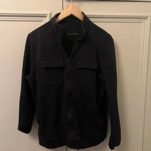 Svart jacka från Massimo Dutti - Snygg svart jacka från Massimo Dutti med dragkedja och två bröstfickor med lock. Jackan har en stilren design och är perfekt för en casual look. Den är långärmad och har en normal passform.
