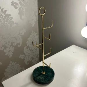 Smyckeshållare i guld och grön marmor - Elegant smyckeshållare med en bas i grön marmor och en ställning i guldmetall. Perfekt för att organisera och visa upp dina smycken på ett stilfullt sätt. Den har flera krokar för att hänga halsband, armband eller örhängen.💕