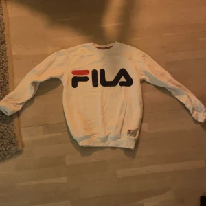 Vit sweatshirt från FILA - Säljer en vit sweatshirt från FILA med deras ikoniska logga i rött och svart på framsidan. Tröjan har långa ärmar och ribbade muddar vid ärmslut och nederkant. Perfekt för en sportig look😮‍💨