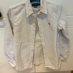 Vit skjorta från Ralph Lauren - Snygg vit skjorta från Ralph Lauren i slim fit. Skjortan har långa ärmar och klassisk krage med knappar framtill. Perfekt för en stilren look.