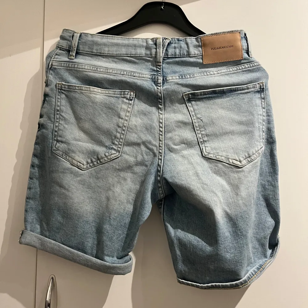 Snygga ljusa jeansshorts från Pull&Bear med slitna detaljer och uppvikta ben. Perfekta för en avslappnad stil. De har klassisk femficksdesign och knappgylf.. Shortsit.