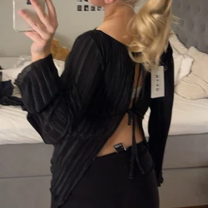 Svart ribbad topp med öppen rygg - Snygg svart ribbad topp från NA-KD med långa ärmar och en stilren design. Toppen har en öppen rygg med knytning. Helt ny, aldrig använd!!🩷🩷Nypris 400kr