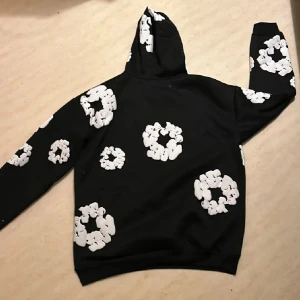 Svart hoodie med vita mönster - Snygg svart hoodie med unika vita mönster över hela tröjan. Den har en klassisk huva och en praktisk magficka framtill. Perfekt för en avslappnad stil. Storlek XL passar även L