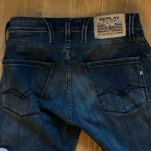 Blå jeans från Replay Modell Anbass  - Snygga blå jeans från Replay i modellen Anbass. De har en slim fit passform och är tillverkade i ett klassiskt denimtyg. Byxorna har en dragkedja och knappar framtill samt stilrena bakfickor. Helt nya använda endast en gång. Pris kan diskuteras 