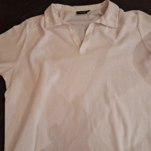 Vit pikétröja från J.Lindeberg - Säljer en stilren vit pikétröja från J.Lindeberg. Tröjan har en klassisk krage och korta ärmar. Storleken är L men liten i modellen, passar M.