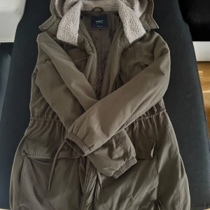 Olivgrön parkajacka från Only - Säljer en olivgrön parkajacka från Only med mysigt teddyfoder i luvan. Jackan har dragkedja och knappar framtill samt praktiska fickor.