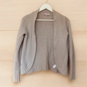 Beige kofta från Butterfly by Matthew Williamson strl S - Stilren beige kofta från Butterfly by Matthew Williamson. Storlek 8 = 36 eller small. Koftan är stickad med en mjuk blandning av nylon, angora och lammull. Den har en öppen design utan knappar och långa ärmar, perfekt för lager-på-lager under kyligare dagar.