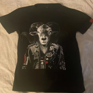 Svart t-shirt med tryck från Replay - Cool svart t-shirt från Replay med ett unikt tryck av en bock i en rockig jacka. T-shirten har korta ärmar och en röd detalj på ärmen med Replay-loggan. Perfekt för en edgy look!