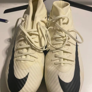 Nike Air Fotbollskor, Med Nike Knäskydd - Snygga beige fotbollsskor från Nike med svart swoosh och snörning. Skorna har en strömlinjeformad design med Air Zoom-teknologi för extra komfort och prestanda på planen. Det finns också knäskydd. De har använts en gång men jag slutade spela fotboll så jag säljer de.