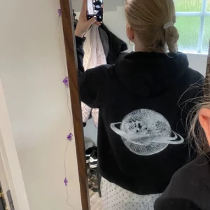 Svart hoodie med planetmotiv - Säljer en svart hoodie med ett coolt planetmotiv på ryggen. Perfekt för en avslappnad stil. Hoodien har långa ärmar och en klassisk passform.