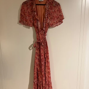 Blommig långklänning från & Other Stories - Säljer en väldigt fin och söt blommig långklänning från & Other Stories. Klänningen har korta ärmar och en omlott-design med knytband i midjan. Använd en gång så den är i väldigt gott skick! Nypris 990