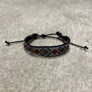 Flätat Armband  - Snyggt vänskapsarmband med ett färgglatt mönster i rött, grönt och svart. Armbandet har justerbara snören för perfekt passform. Sjukt snyggt och väldigt eftertraktat. Vid minsta fråga eller fundering hör av er🤝
