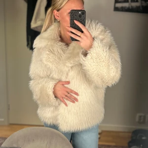 Beige pälsjacka - Säljer en fluffig och stilren beige pälsjacka med långa ärmar. Perfekt för att hålla sig varm och trendig under kyliga dagar. Jackan har en klassisk design som passar till många olika outfits.