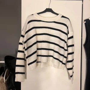 Vit och svart randig stickad tröja - Säljer en stilren vit stickad tröja med svarta ränder. Tröjan har långa ärmar och en bekväm passform. Perfekt för en avslappnad look.