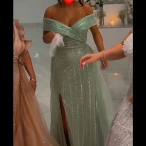 Mintgrön glittrig festklänning - Elegant grön festklänning med glittrande detaljer med ett släp och en slits framtill. Perfekt på bröllop eller till bal🥰 Köpte den på rever design i Södertälje, använd en kväll. Är 163cm, var perfekt i längden med 7cm klack. Passade mig som är en S/36. Kan sys in i midjan och sys upp i längden. Pris kan diskuteras vid smidig affär.♥️