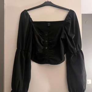 Svart blus med knappar - Snygg svart blus från H&M med långa puffärmar och knappar framtill. Perfekt för en stilren look.