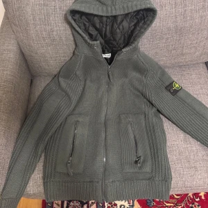 Grön Stone Island stickad jacka med huva - Säljer en grön stickad jacka från Stone Island med huva och dragkedja. Jackan har två fickor med dragkedjor och ett quiltat foder. Perfekt för kyliga dagar. Bara att skicka ett meddelande om man har några frågor. Priset går alltid att diskutera, sitter bra på mig som är storlek M men passar även folk i storlek S.