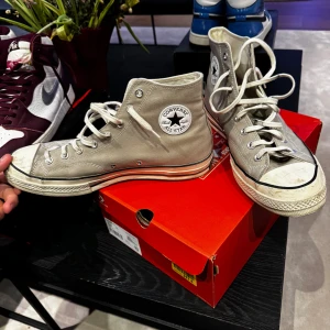 Grå Converse All Star Chuck Taylor - Säljer ett par klassiska grå Converse All Star Chuck Taylor med hög snörning och den ikoniska logotypen på sidan. 