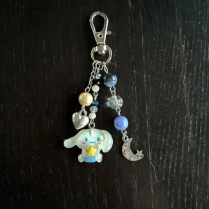 Nyckelring med figur och pärlor - Charmig nyckelring med en söt figur som håller en stjärna. Nyckelringen har även pärlor i olika färger och en silverfärgad måne och hjärta. Perfekt som accessoar för att ge en personlig touch till dina nycklar eller väska.