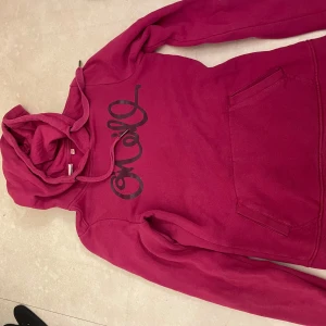Rosa hoodie med tryck - Säljer en snygg rosa hoodie med svart tryck på framsidan. Den har en klassisk känguruficka och justerbar huva med snören. Perfekt för en avslappnad stil.
