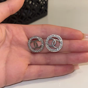 Silverfärgade örhängen med glittriga detaljer - Snygga silverfärgade örhängen med glittriga stenar runt en cirkulär design. Perfekta för att ge en touch av elegans till din outfit. De har en klassisk och tidlös stil som passar till många tillfällen.