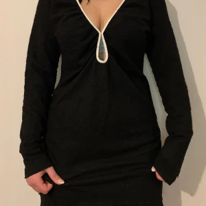 Svart långärmad klänning med v-ringning - Snygg svart klänning med lång ärm och djup v-ringning. Perfekt för en stilren look. Klänningen har en smickrande passform och är enkel att matcha med olika accessoarer.