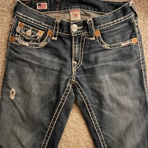 Blå jeans - True Religion - Tjo, Säljer ett par blå jeans från True Religion då jag köpte en kvinnomodell med bootcut som jag personligen it skulle vilja bära. Trueysen har slitna detaljer och kontrastsömmar. Modellen är Billy Super T och har en klassisk femficksdesign med knappar och broderade bakfickor. 