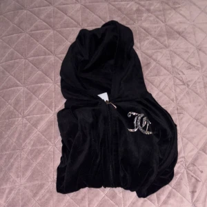 Svart velourset från Juicy Couture - Säljer ett svart velourset från Juicy Couture med glittrande detaljer. Setet består av en långärmad hoodie med dragkedja och matchande byxor. Perfekt för en avslappnad och stilren look. 🖤✨Byxorna har fickor fast utan knappar! Bra skick