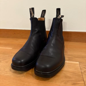 Svarta boots från Blundstone - Snygga svarta boots från Blundstone i skinn. De har en klassisk design med elastiska paneler på sidorna och dragflikar för enkel påtagning. Perfekta för en stilren look. Modellen Dress CHISELED TOE BOOT. Stl 4. Motsvarar stl 37, men så här skriver Blundstone själva om stl: Överväg att gå ner en halv eller till och med en hel storlek, särskilt om du har en smal fot. Sparsamt använda - vilket syns på sulorna. Nypris 2200:-  Vattentäta skor. 