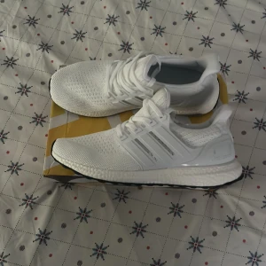 Vita Adidas Ultraboost sneakers - Snygga och bekväma vita Adidas Ultraboost sneakers med stickad ovandel och klassisk Boost-sula. Perfekta för både träning och vardag.  Har använt de två dagar i gymmet. Säljer de för att de sitter tajt på mig. Priset kan diskuteras 